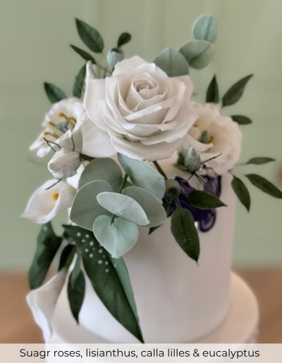 Sugar flowers including white roses, lisianthus, calla lilies and eucalyptus on a wedding cake