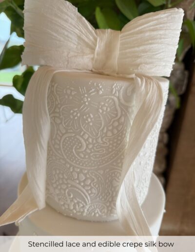 Close-up of stencilled lace detailing and edible crepe-silk bow on a bespoke wedding cake for Hazel Gap Barn