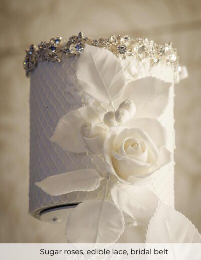 Top tier of a luxury wedding cake with handcrafted sugar roses, edible lace texture and bridal belt detail
