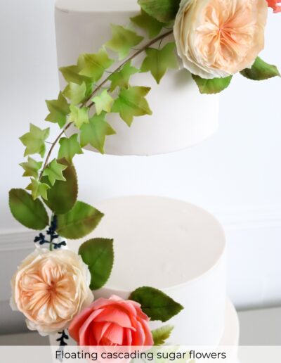 Floating ivory wedding cake tiers decorated with peach and coral sugar roses, trailing ivy and handcrafted foliage.