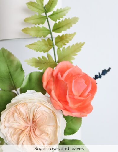Close-up of peach and coral sugar roses with handcrafted green leaves and fern foliage.