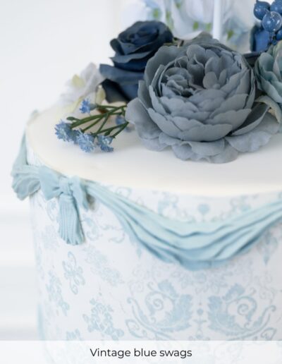 Powder blue wedding cake decorated with damask patterns, sugar swags, tassels and blue flowers.