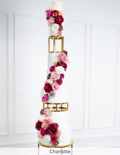 Tall ivory wedding cake with gold geometric spacers and cascading pink, burgundy and white flowers.
