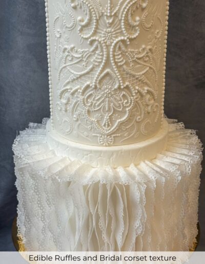 Ivory wedding cake with intricate bridal lace piping and pleated edible ruffle details.