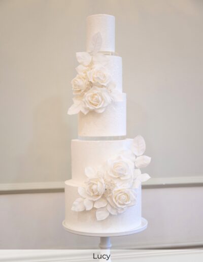Tall sparkling white wedding cake with clear acrylic spacers and arrangements of handcrafted white sugar roses at Owston Halll Doncaster