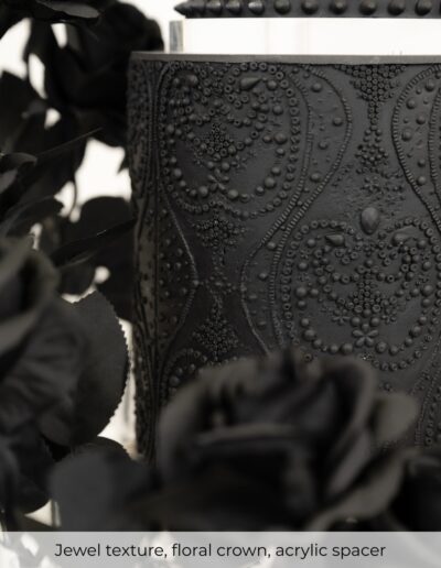 Black wedding cake tier with jewel-inspired texture, black sugar roses and a clear acrylic spacer.