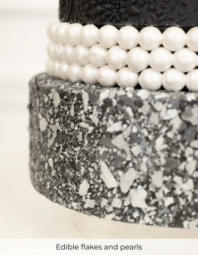 Black and white wedding cake detail with edible stone-effect flakes and rows of pearl-like decorations.