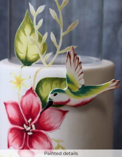 Hand-painted tropical flowers and green leaves with a raised colourful hummingbird on an ivory wedding cake tier.