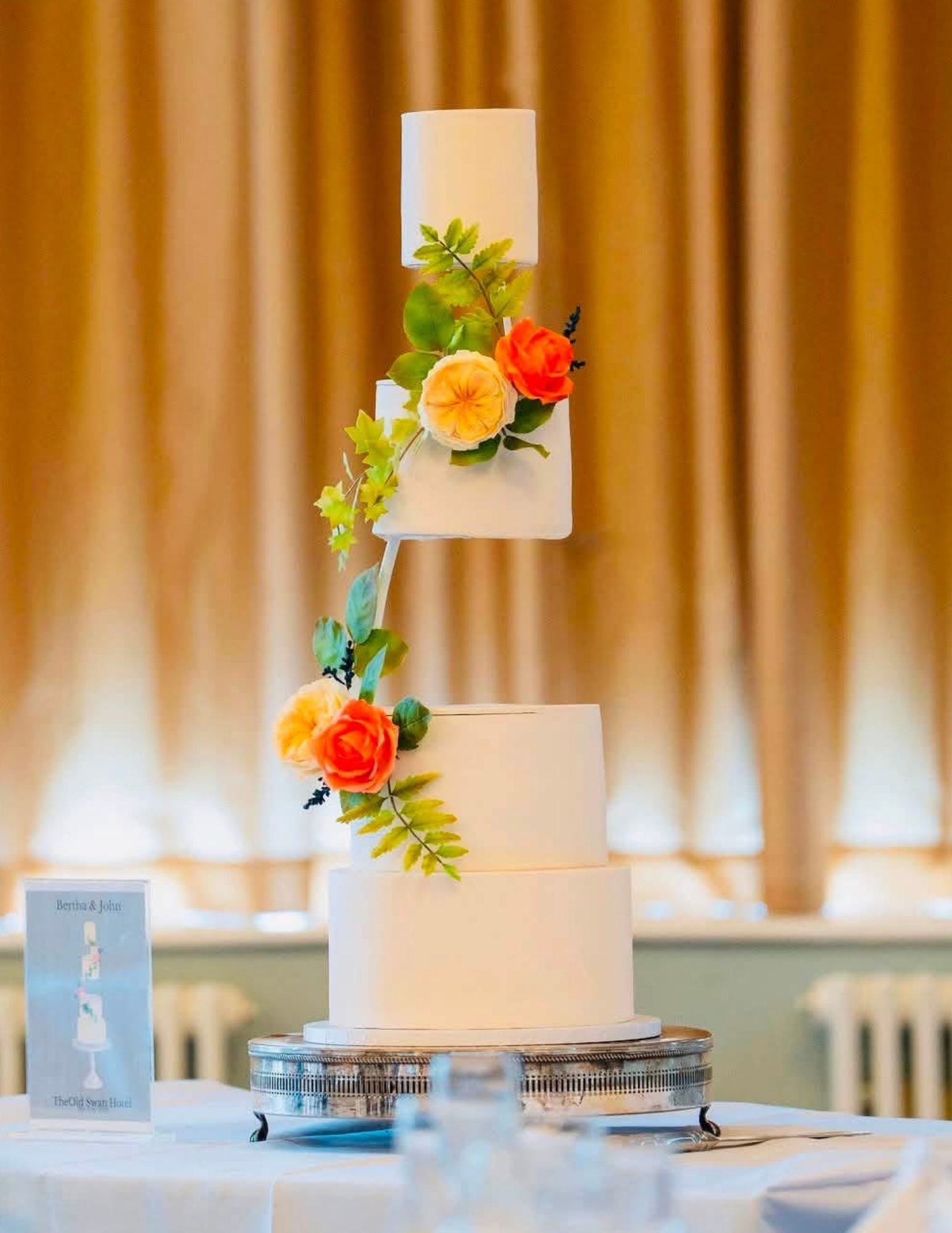 Modern tiered wedding cake with handcrafted orange sugar roses and foliage at The Old Swan Hotel.
